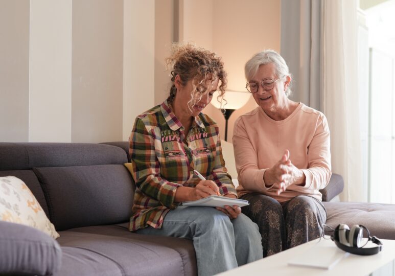 Smiling,senior,woman,and,caregiver,sharing,a,moment,sitting,together